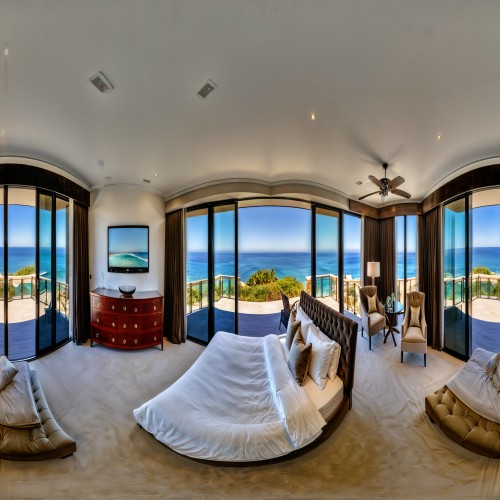 An elegant master bedroom with a plush king-size bed, velvet upholstered headboard, and glass doors leading to a private balcony overlooking the ocean.