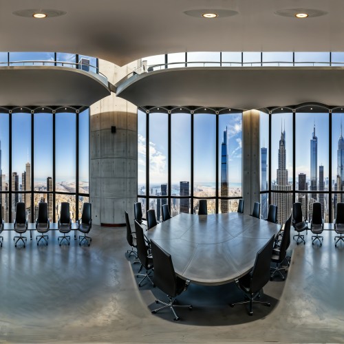 A spacious modern conference room with a polished concrete table, ergonomic chairs, and a wall-to-wall window offering a skyline view.