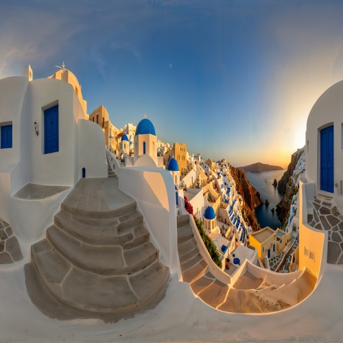 Scenic View of Santorini, Greece: Whitewashed buildings with blue-domed roofs overlook the sparkling Aegean Sea in Santorini. The iconic architecture is bathed in warm evening light, with winding staircases and balconies adding charm to the cliffside village.